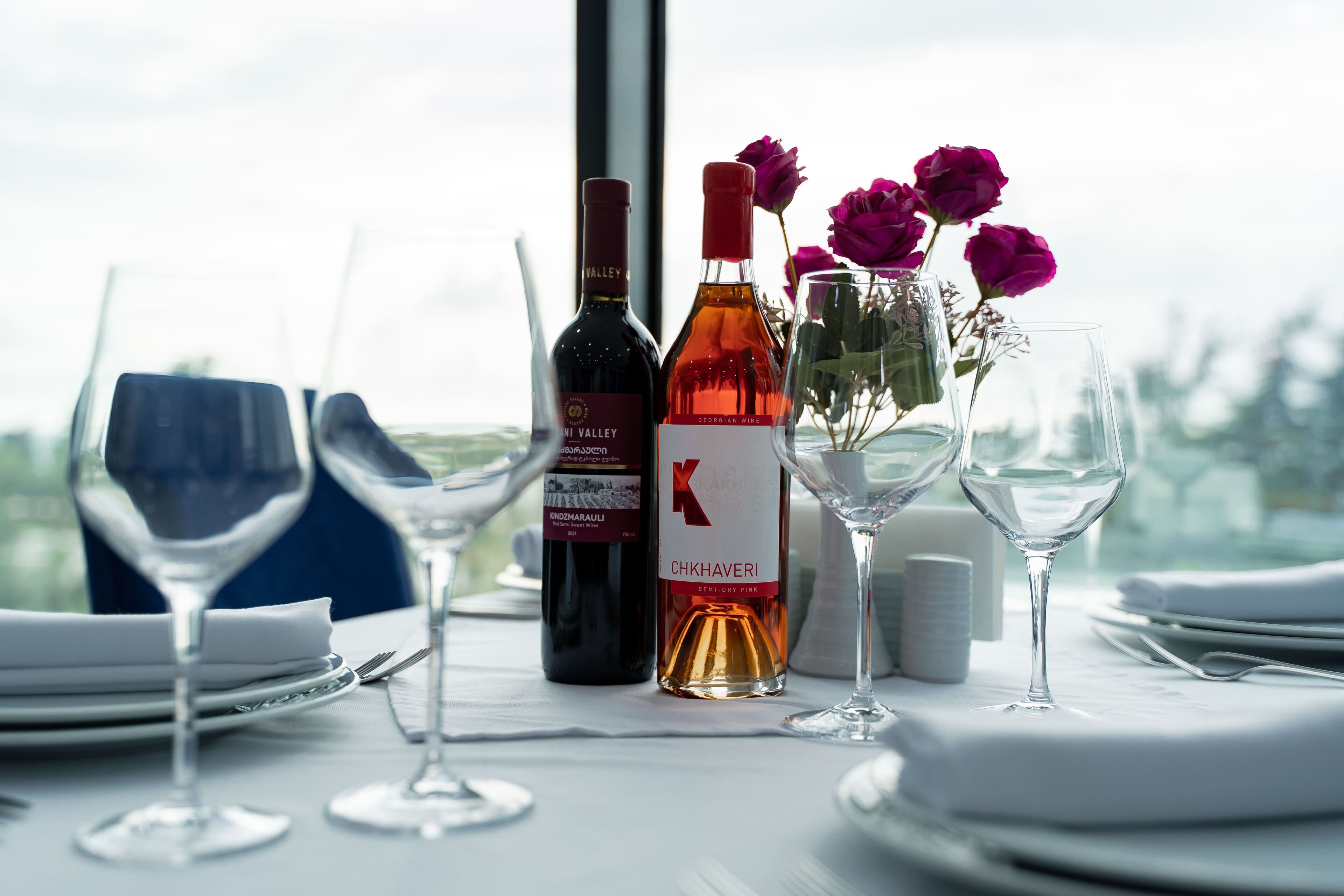 Une table mise pour le dîner, avec des bouteilles de vin et un vase de fleurs.