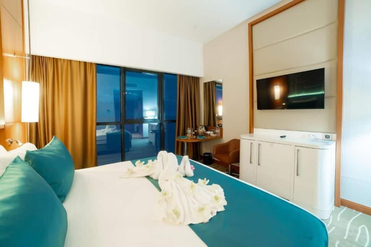 A hotel room with a bed, a desk, a television, and a view of the outside.