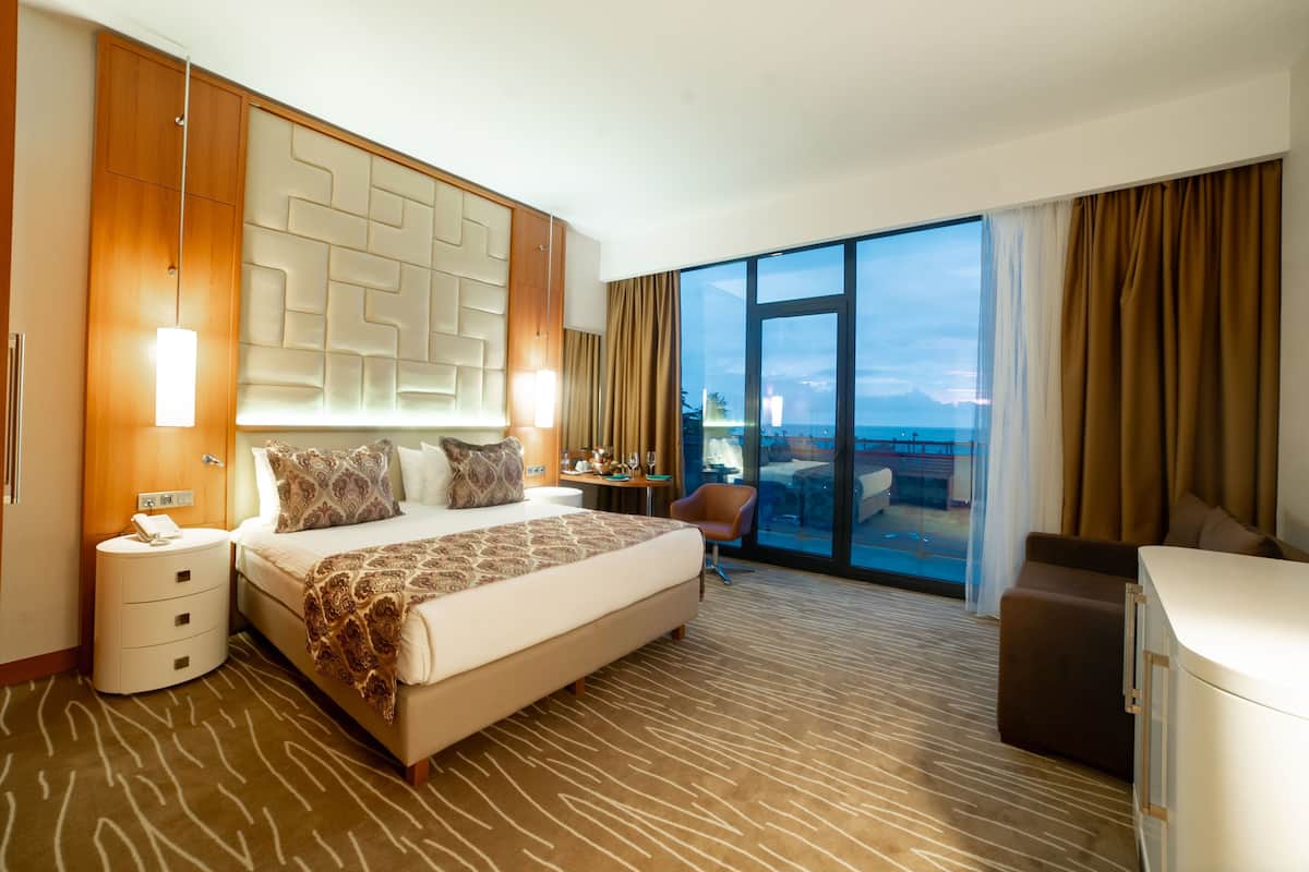 A modern hotel room with a large bed, a desk, a chair, and a view of the ocean.
