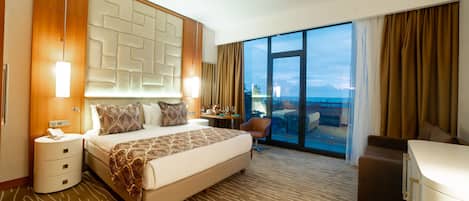 Una habitación de hotel moderna con una cama grande, un escritorio, una silla y vista al océano.