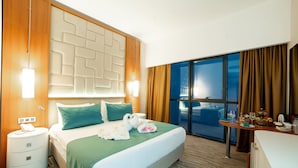 A hotel room with a large bed, a nightstand, a desk, and a view of the city through the window. -  Grand Bellagio Batumi Convention & Casino Hotel (Batumi)