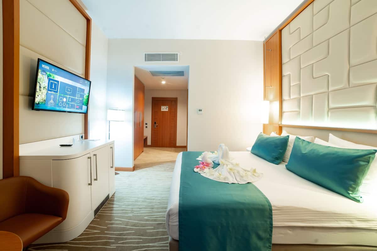 A hotel room with a bed, a TV mounted on the wall, a desk with a chair, and a door leading to another room.