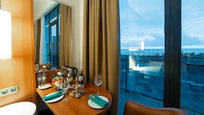 A hotel room with a dining table set for two, a minibar, and a large window offering a view of a cityscape and a bridge. -  Grand Bellagio Batumi Convention & Casino Hotel (Batumi)