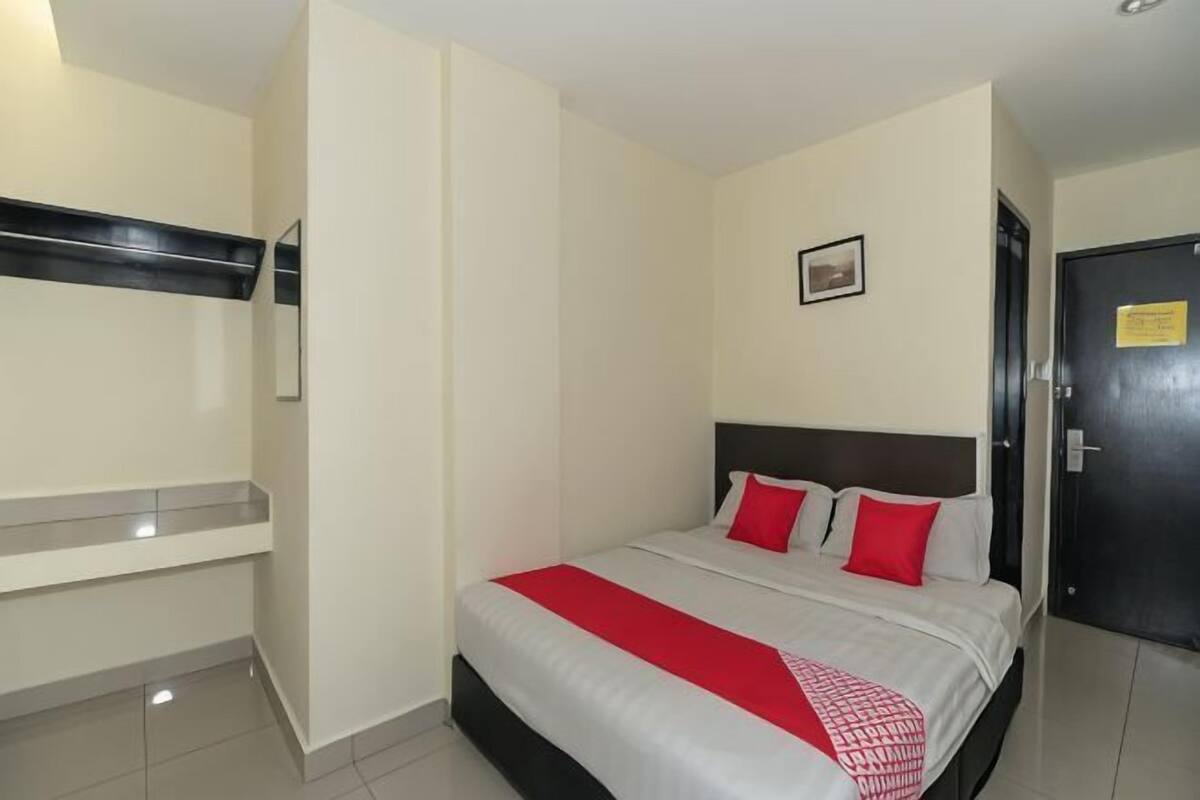 A hotel room with a bed, a bedside table, a mirror, a door, and a wall-mounted shelf.