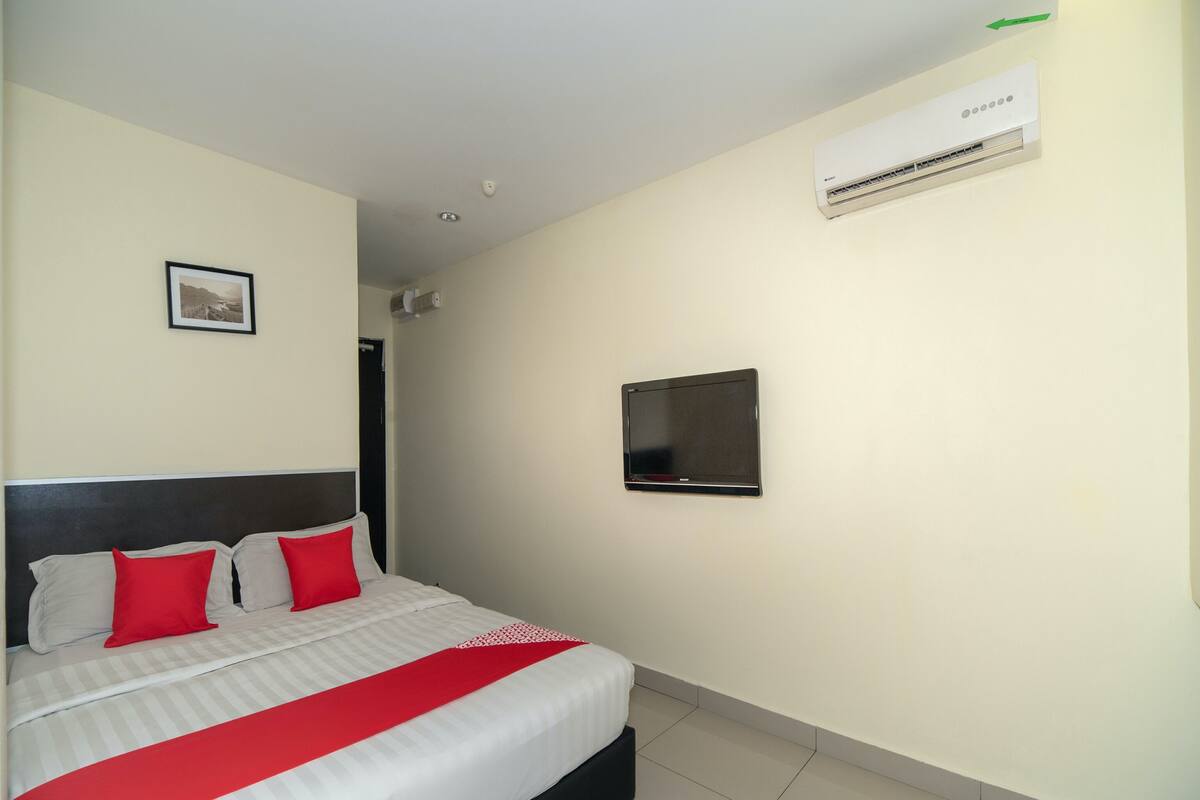 A hotel room with a bed, a flat-screen TV mounted on the wall, and an air conditioning unit above the TV.