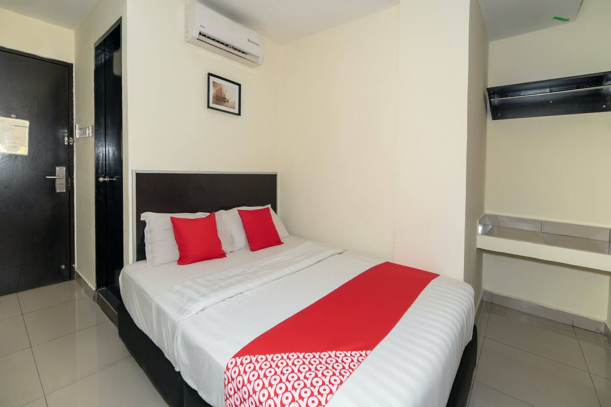 A hotel room with a bed, a black door, an air conditioning unit, a framed picture on the wall, and a bunk bed against the wall.