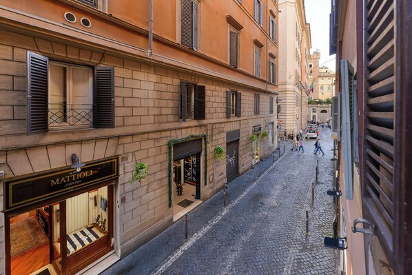 A cobblestone street with historic buildings, a visible storefront with a sign, and a pedestrian walkway.