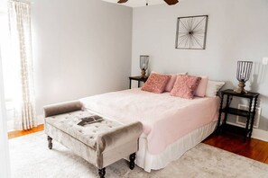Une chambre à coucher avec un lit, une table de chevet, une lampe, une chaise et une fenêtre avec des rideaux.