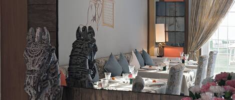 A dining area with a large mirror reflecting the room, a table set for four, and decorative items including a vase of flowers and elephant figurines.