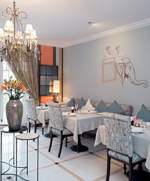 A dining area with a chandelier, patterned chairs, and a wall mural. - The Rohet House (Jodhpur)