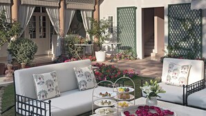 Un patio con un conjunto de sofá blanco, una mesa con servicio de té y plantas en macetas.
