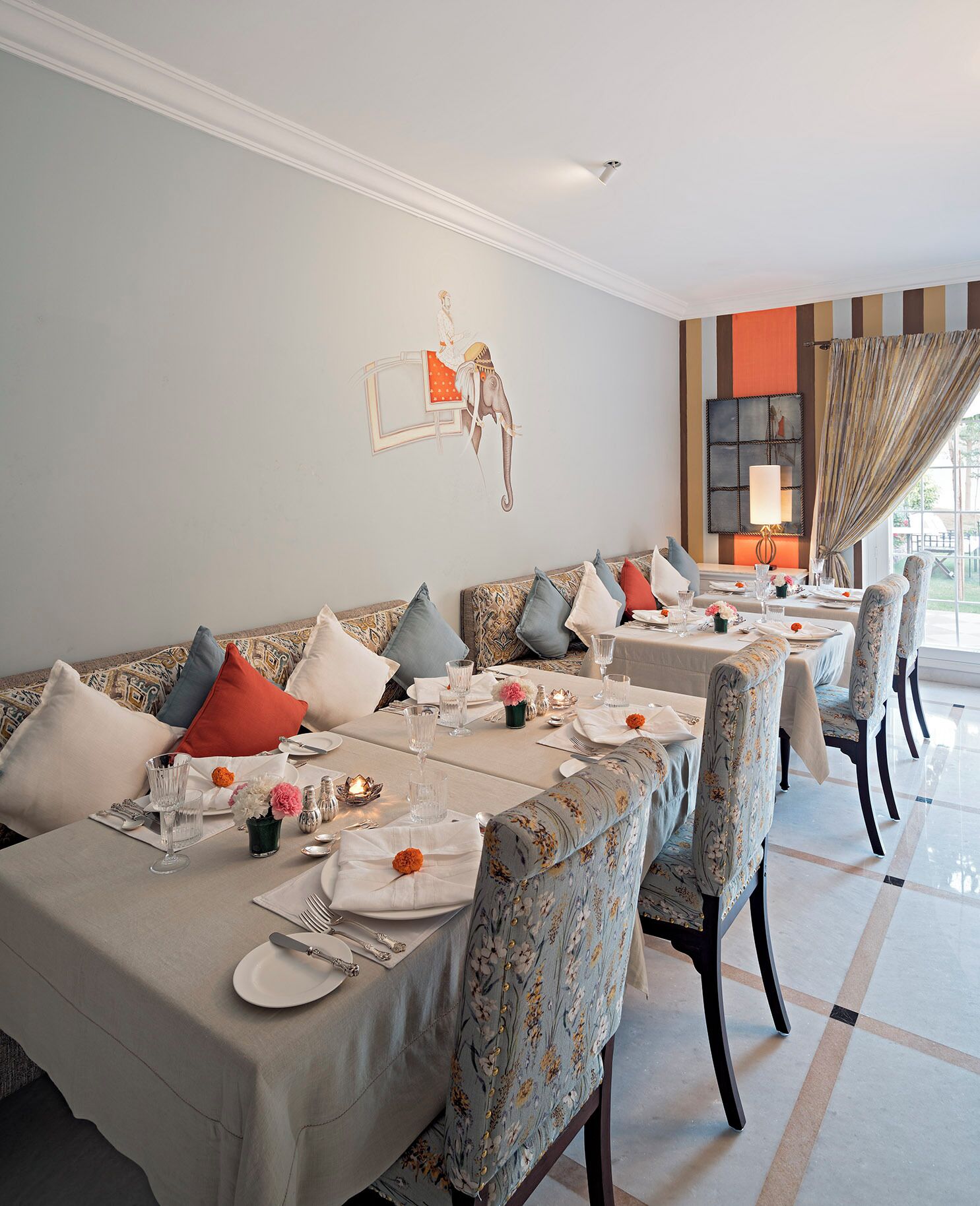 Un comedor con una larga mesa dispuesta para una comida, flanqueada por sofás y sillas con diseño decorativo.