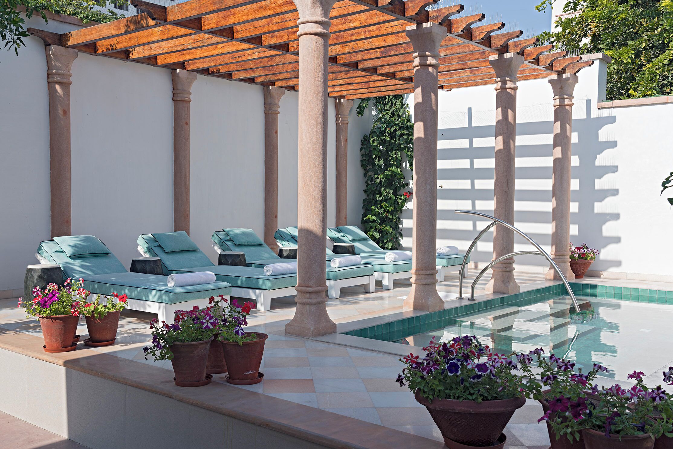Un área junto a la piscina con sillones de descanso, una pérgola y plantas en macetas.