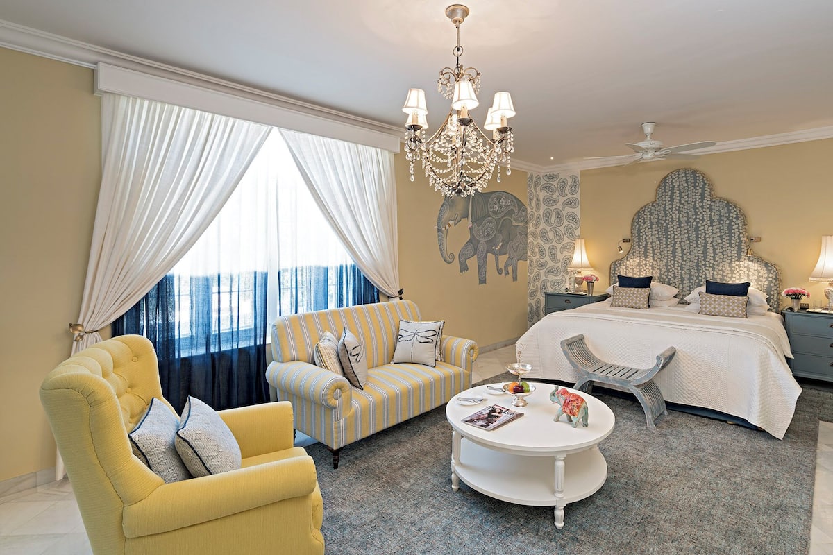 A bedroom with a bed, a sofa, a chair, a coffee table, and a chandelier.