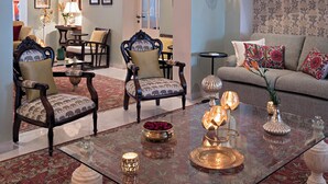 Amplia sala de estar con una gran lámpara de araña, sillas ornamentadas, un sofá y una mesa de centro con objetos decorativos.