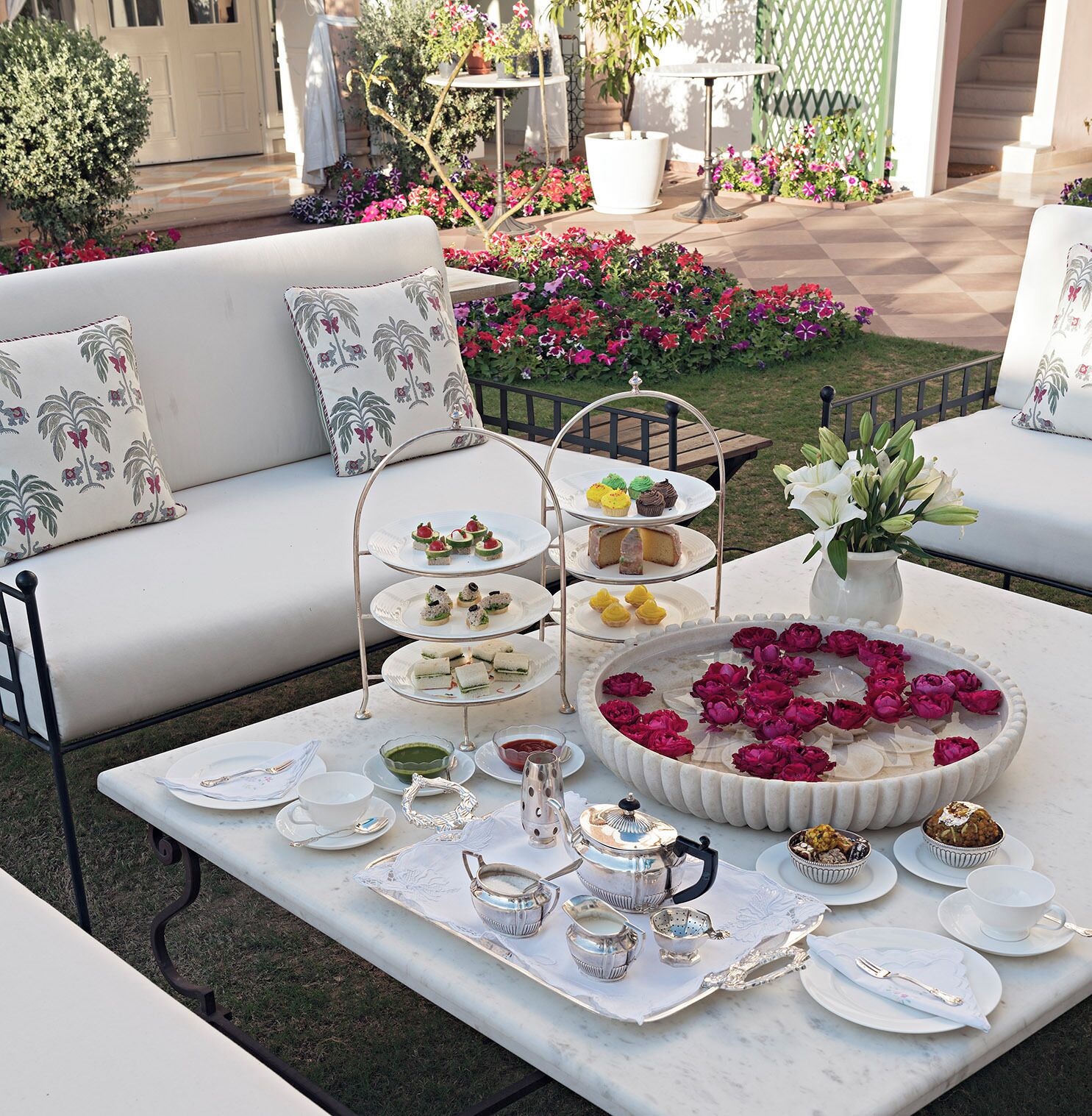 Un espacio de estar al aire libre con un sofá blanco, una mesa con un soporte escalonado para postres, y un arreglo floral.