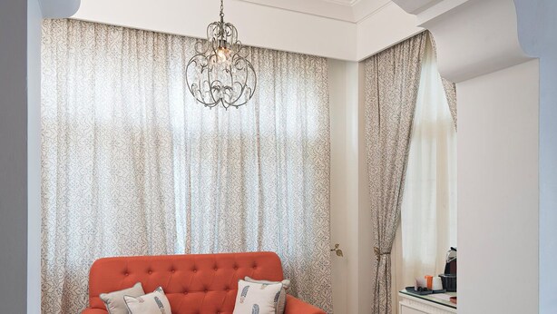 A modern living room with a red sofa, patterned curtains, a glass coffee table, and a chandelier. - The Rohet House (Jodhpur)