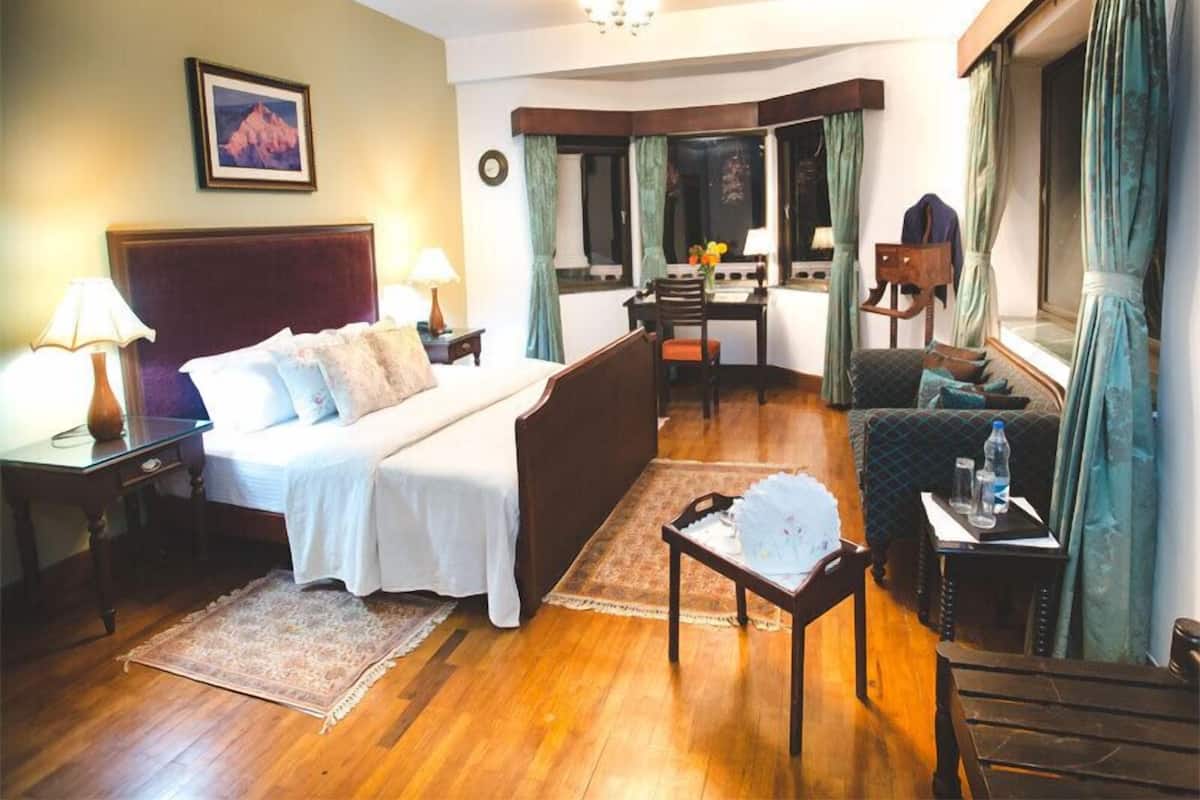 Een hotelkamer met een bed, een bureau, een stoel, een bijzettafeltje en een raam met gordijnen.