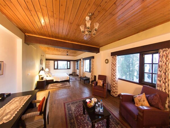 Un salon spacieux doté d’un plancher en bois, d’une grande fenêtre avec des rideaux, d’un canapé, d’une table basse et d’un coin repas avec une table et des chaises.