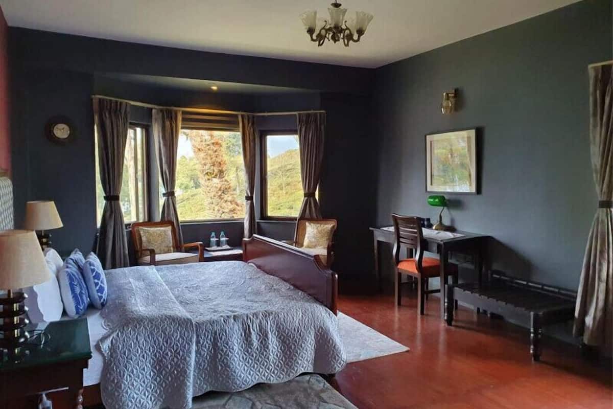 Een slaapkamer met een groot bed, een bureau en stoelen. Er zijn gordijnen voor de ramen en een kroonluchter hangt aan het plafond.
