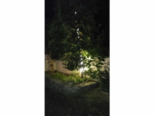 Un jardín con un banco de piedra y una pared, iluminado por pequeñas luces.