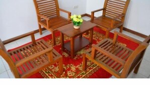 Una habitación de esquina con una mesa de madera y cuatro sillas, un tapete rojo estampado y una pequeña planta en maceta sobre la mesa.