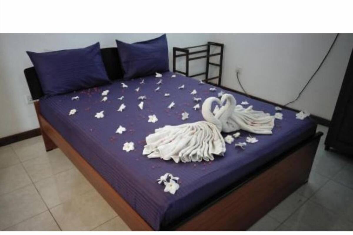 A bed with a purple bedspread, white flowers, and a towel arranged in a swan shape.