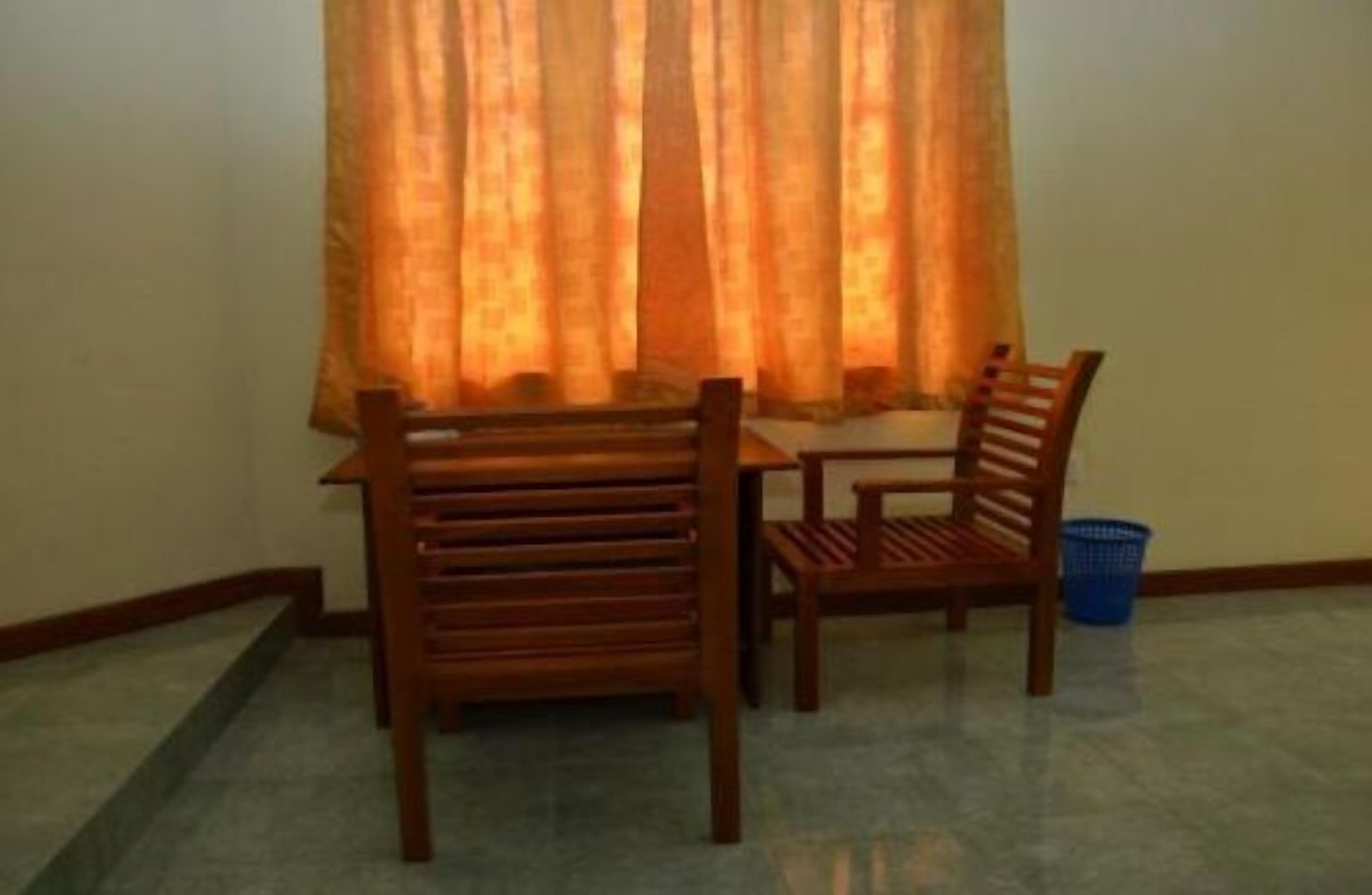 A room with a wooden table and two chairs, a blue basket, and a window with orange curtains.