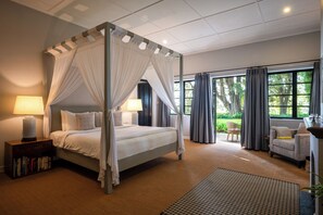 A four-poster bed with white linens, a bedside table with a lamp, and a bookshelf.