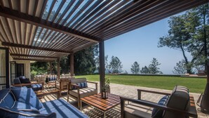 Ein überdachter Außenbereich mit Sofas, Sesseln, einem Holztisch und Blick auf die Landschaft.