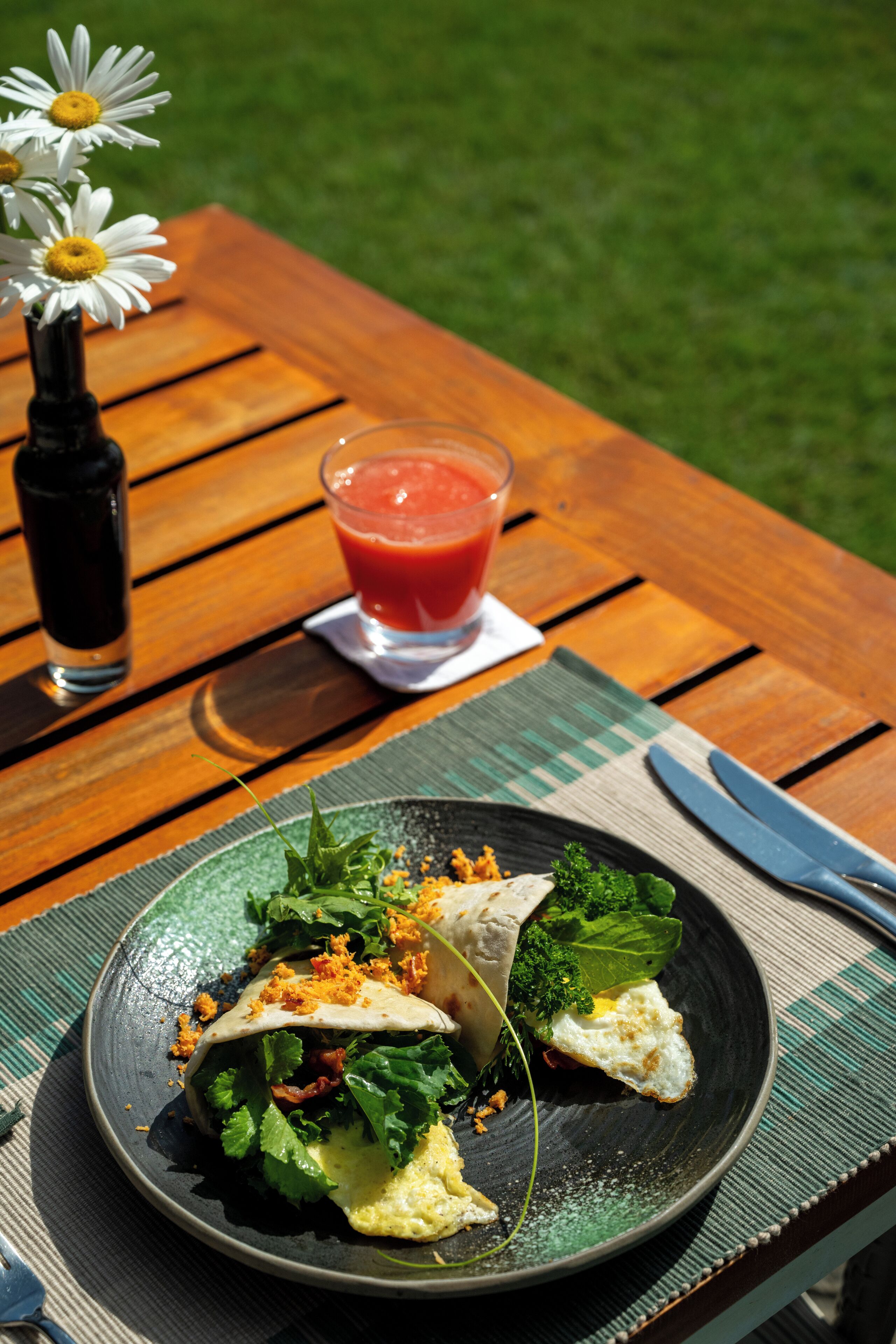 Une table en bois, avec une assiette de nourriture, un verre d’une boisson rouge et une bouteille.
