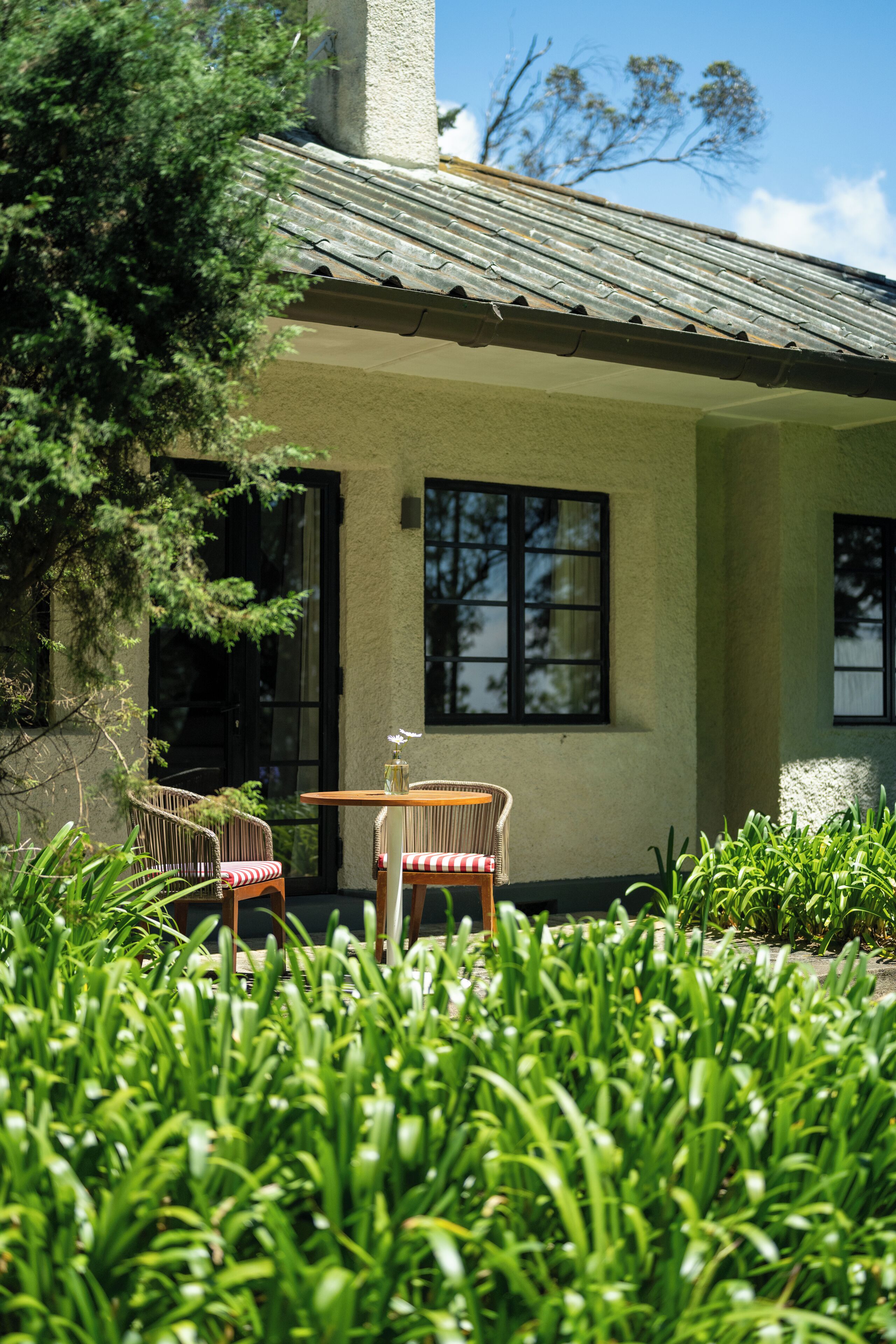 A building with a tiled roof, two windows, and a small patio area with a table and chairs.