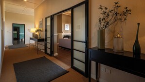 Ein Flur mit einer Schiebetür zu einem Zimmer, einem kleinen Tisch mit einer Lampe und einer Vase mit Zweigen auf einer Anrichte.