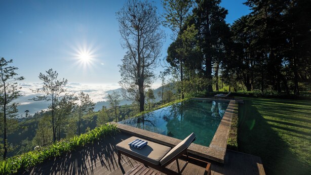 Ein Pool ohne Ende mit einer Holzterrasse, Liegestühlen und Blick auf eine Berglandschaft.