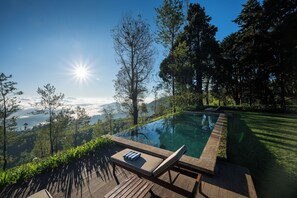 An infinity pool with a wooden deck, lounge chairs, and a view of a mountainous landscape.