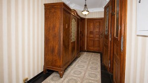 Un pasillo con papel tapiz a rayas, un armario de madera, una alfombra estampada y una puerta con placa de número.