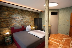 Ein Schlafzimmer mit Steinwand, einem Bett mit rotem Kopfteil, einer Holzsäule und einer Tür.