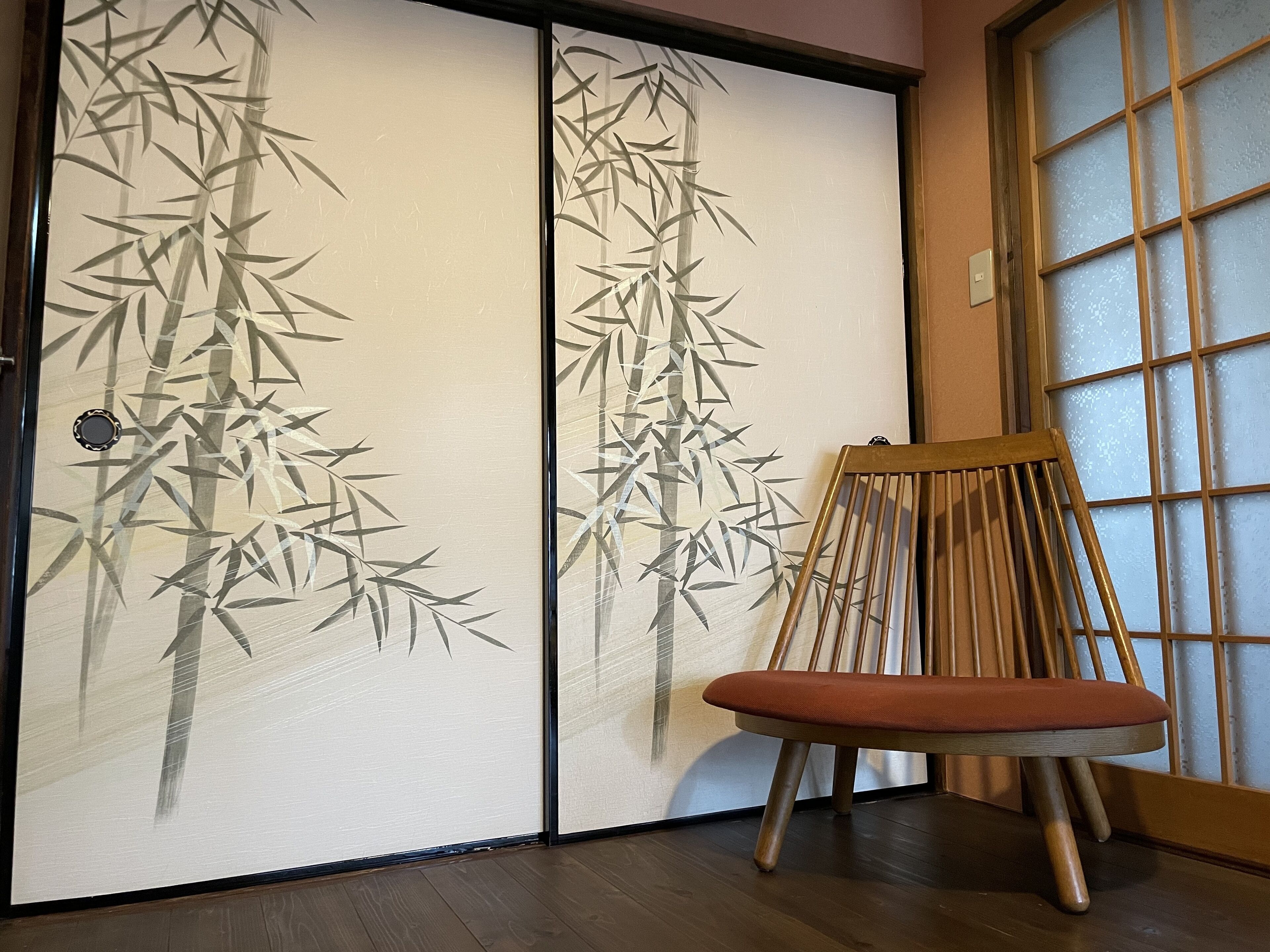 Una habitación con puertas correderas que exhiben arte con bambú, una silla de madera con cojín y suelo de madera.