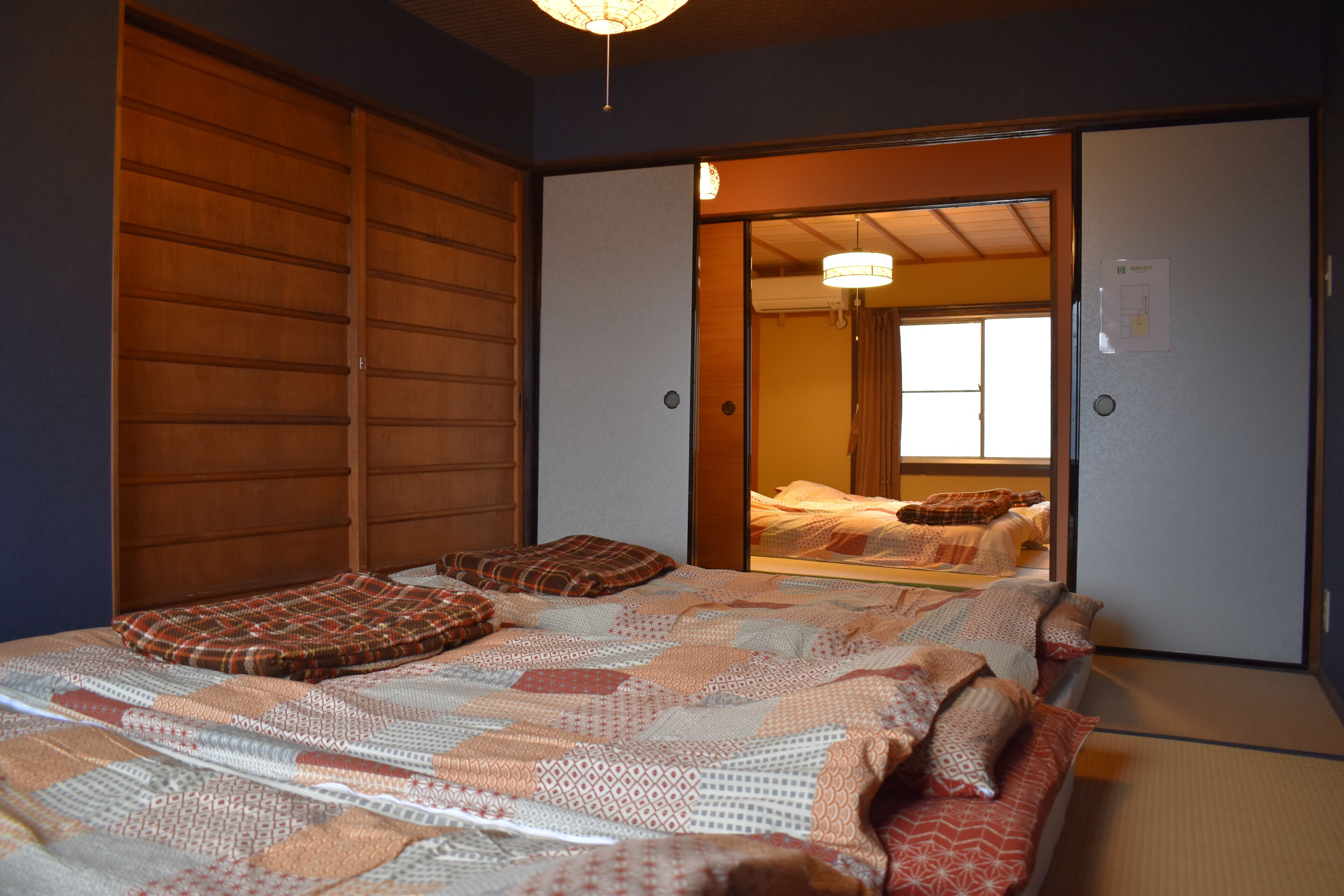Une chambre de style japonais traditionnel, avec un sol recouvert de tatamis, un grand lit doté de nombreux oreillers et des portes coulissantes donnant sur une autre pièce.
