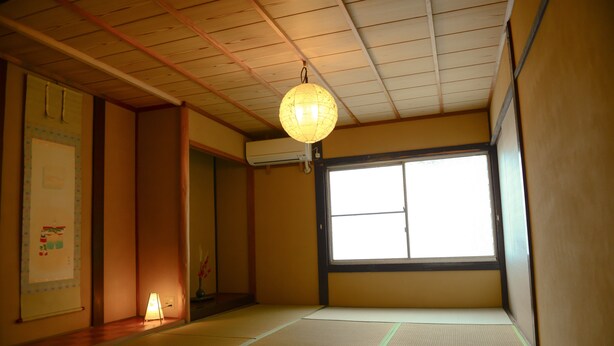Una tradizionale stanza giapponese con pavimento in tatami, paravento shoji e lanterna di carta sospesa.