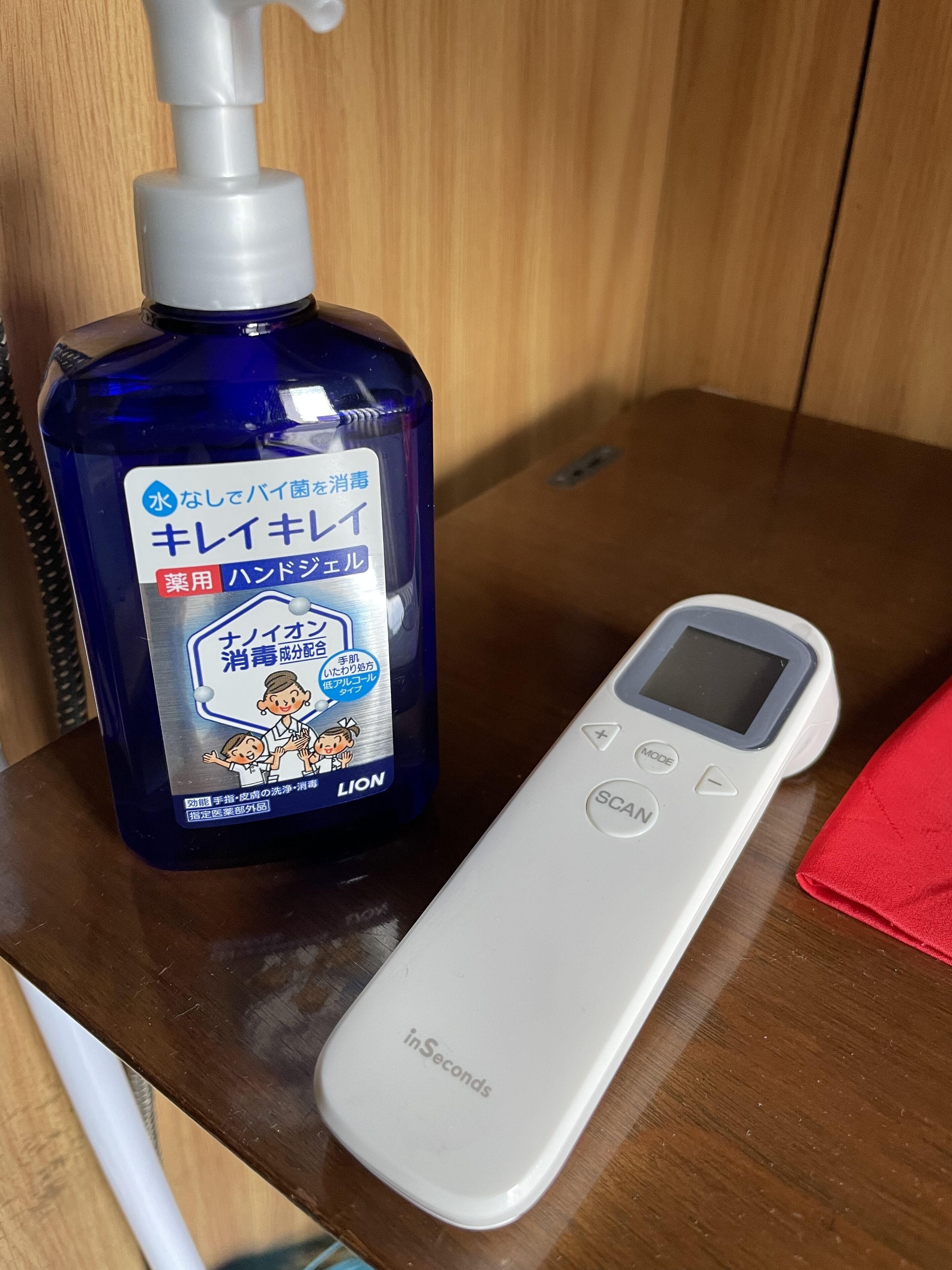Sininen pullo käsidesiainetta ja valkoinen inSeconds-merkkinen digitaalinen lämpömittari puupinnalla.
