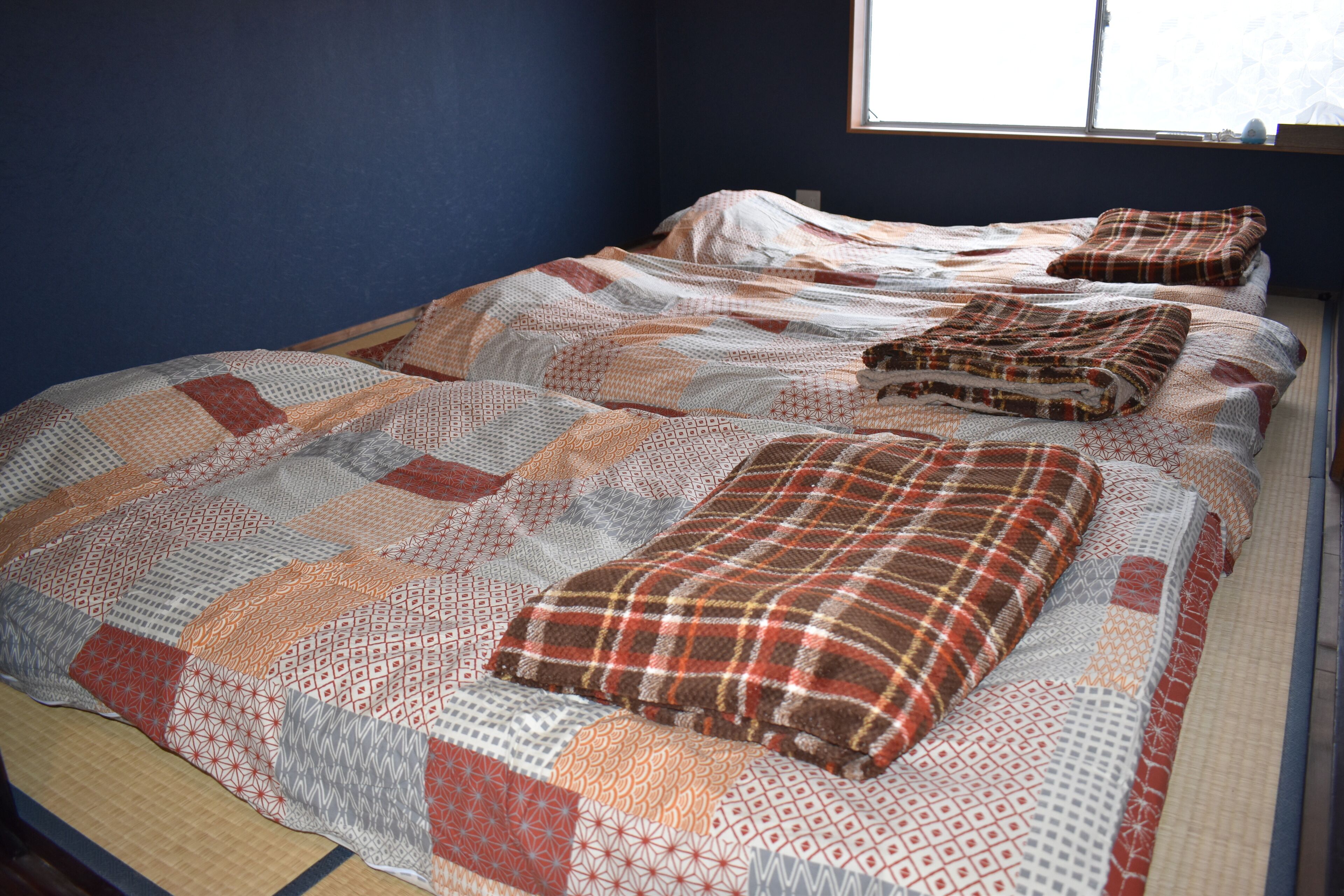A bed with a patterned quilt and pillows, a window with a view, and a blue wall.