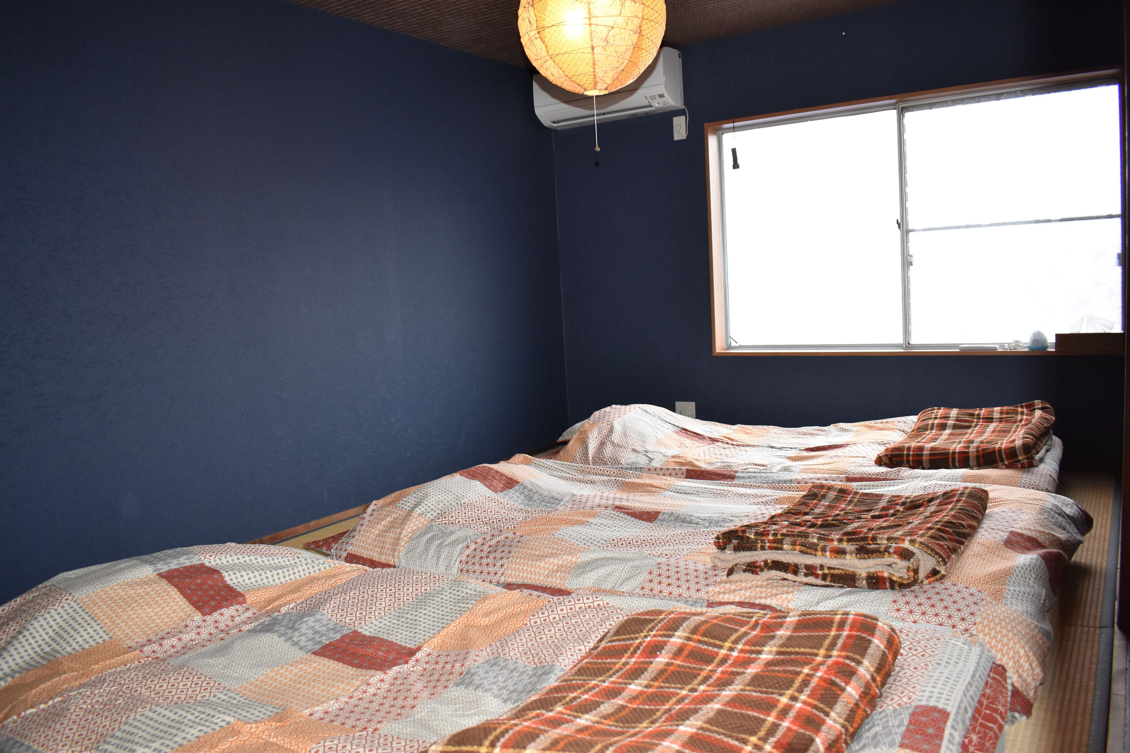 Une chambre à coucher avec un grand lit recouvert d’une literie à motifs, une fenêtre avec des stores et un ventilateur de plafond.