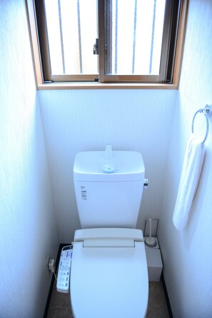 A small, white bathroom with a toilet, a bidet, and a window above the toilet.