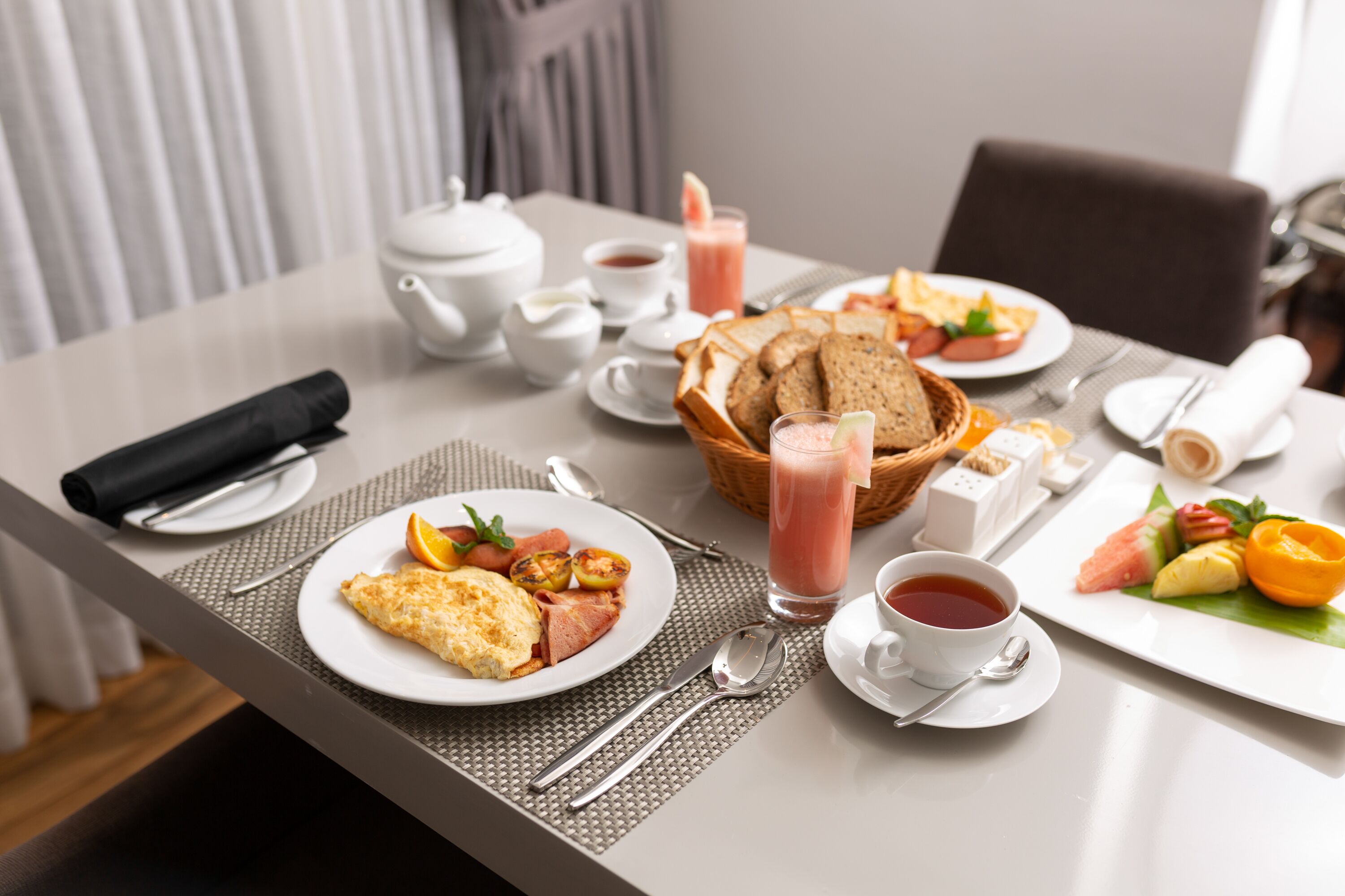 A breakfast setting with plates of food, a teapot, cups, and a basket of bread.
