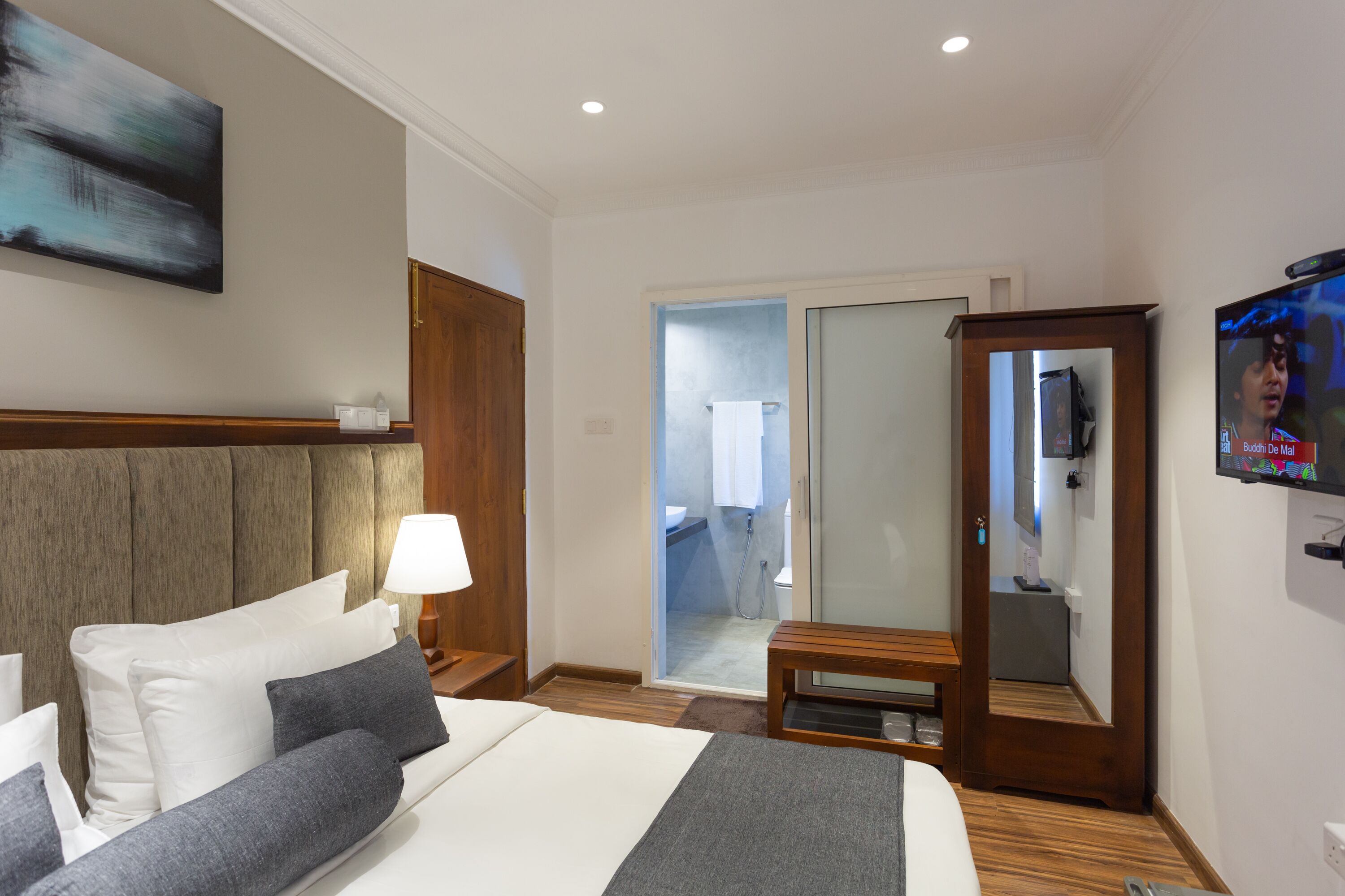 A hotel room with a bed, a television, a mirror, and a bathroom door.