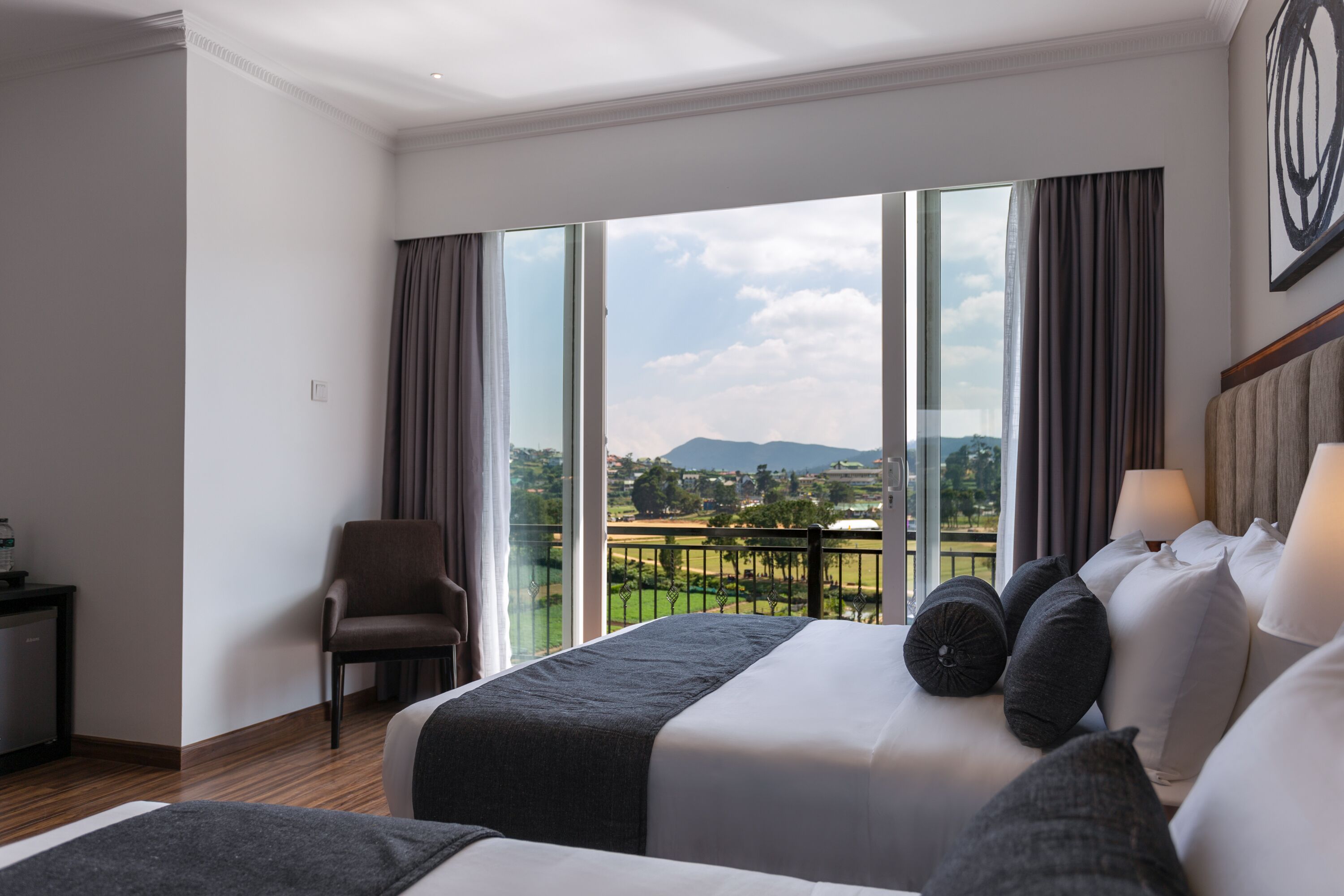 A hotel room with a large window, a bed, a chair, and a desk.