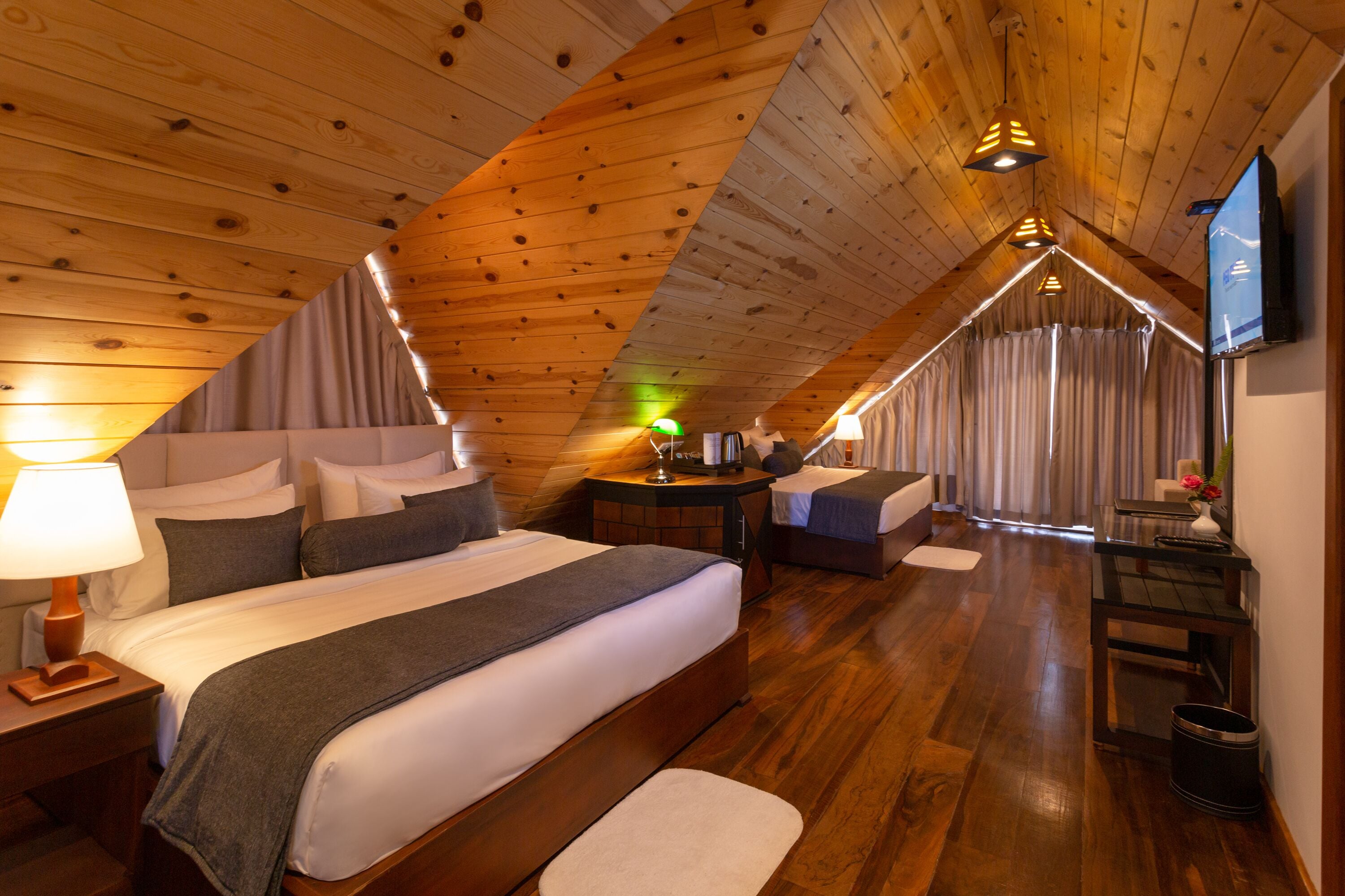 A cozy, wooden-paneled room with a large bed, a small seating area, and a television on the wall.