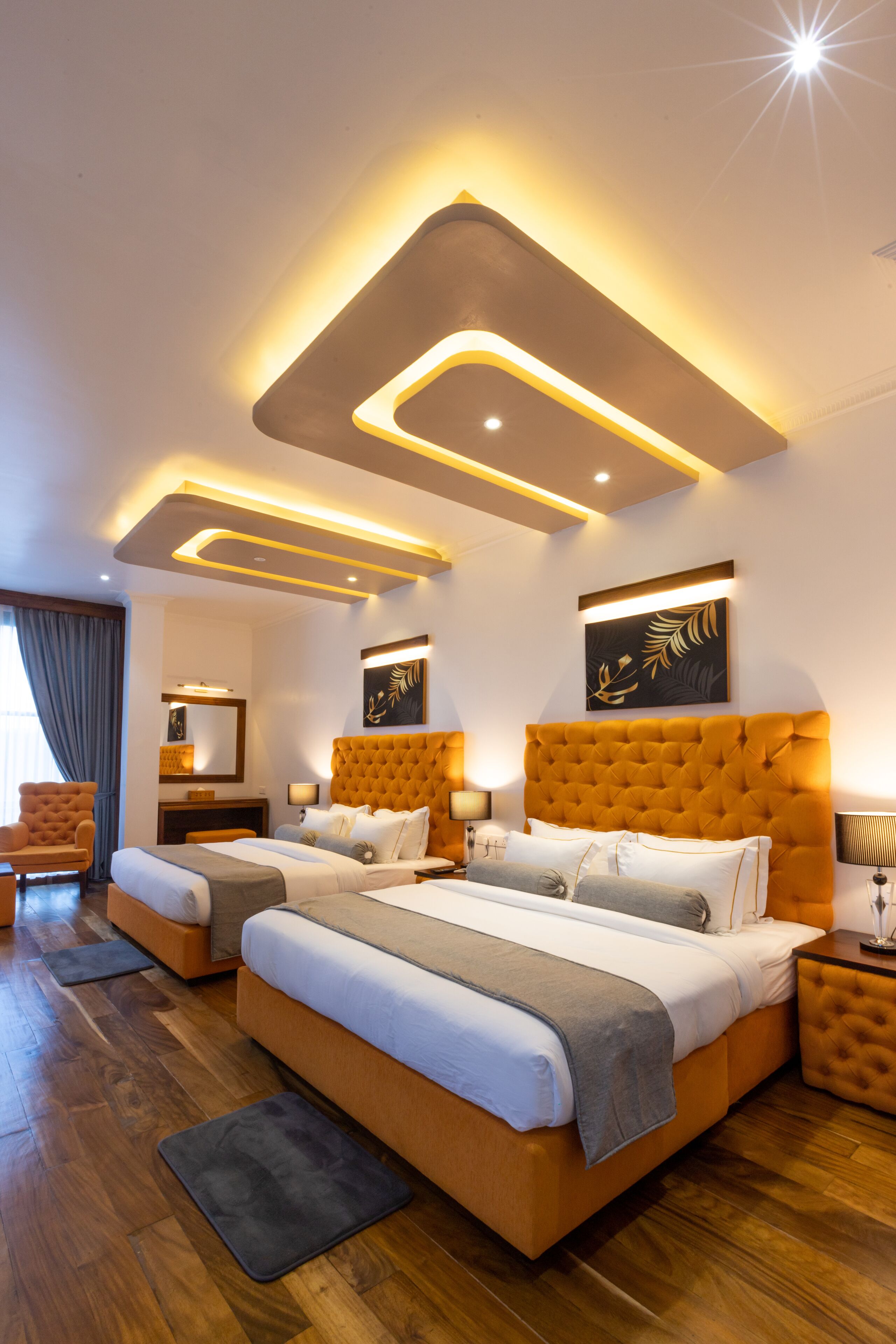Habitación de hotel moderna con una cama grande, dos mesitas de noche, una silla y un ventanal con cortinas.