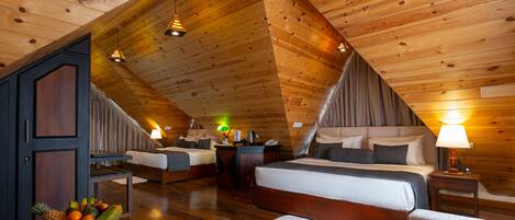 A cozy attic bedroom with wooden ceilings, two beds, a desk, and a fruit basket.